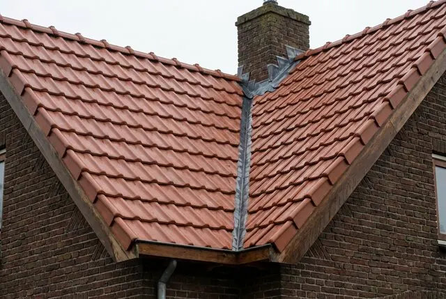 Hellend dak met nieuwe keramische dakpannen en loodwerk bij de schoorsteen