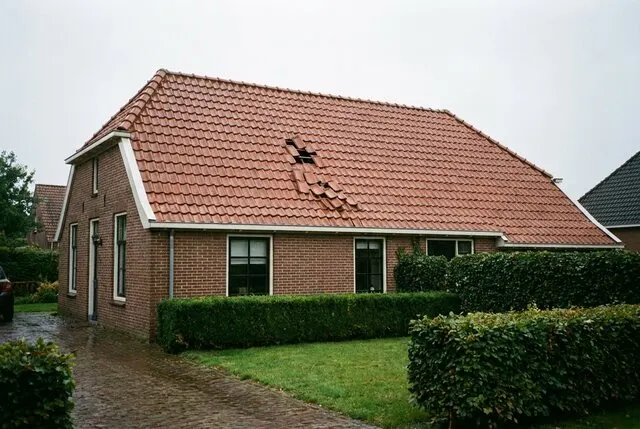 Pannendak van een woning waar een paar pannen bij de nok verschoven zijn en er een ontbreekt