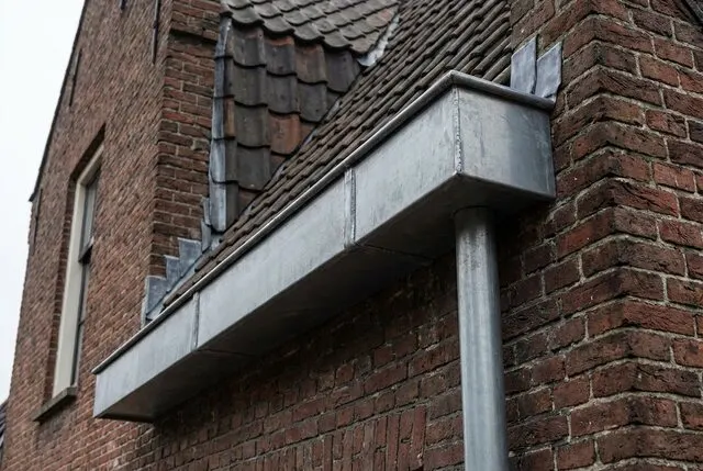 Zinken bakgoot met soldeernaad langs de gevel van een bakstenen pand